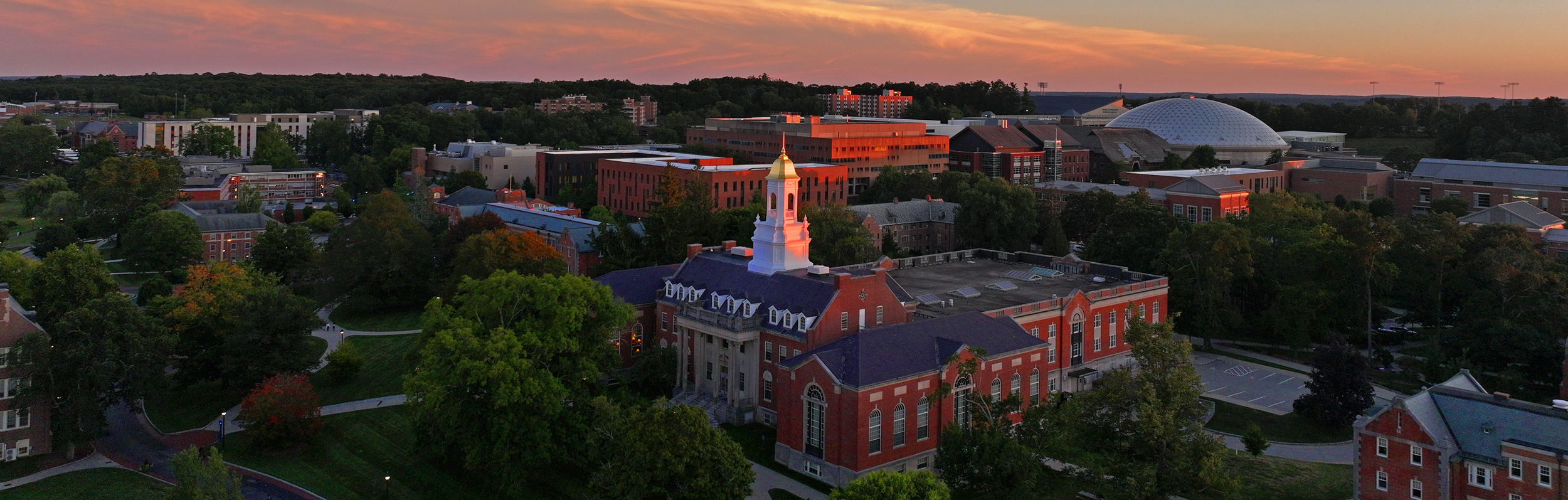 Sunset over a college campus with logs of brick building and a dome in the background.
