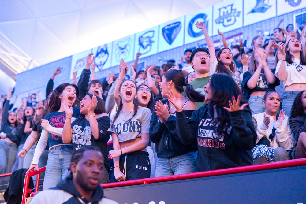 Crowd of UConn fans cheering in the stands at an indoor event.