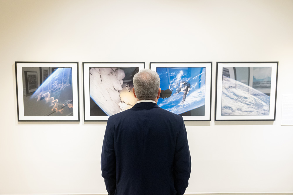 A person stands in front of a gallery wall viewing four framed photographs of Earth and space, each showing different atmospheric and orbital perspectives.